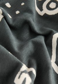 Dark green fabric with a soft texture featuring white abstract patterns and shapes, including circles and dashes, with varied thicknesses.