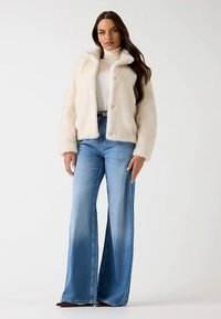 Short cream faux fur jacket with a collar and three buttons paired with high-waisted light blue flared jeans. Smooth texture and relaxed fit.