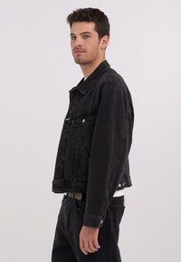 Sort denimjakke med krave, forlommer og knaplukninger. Har en cropped skæring og glat tekstur. Stylet med sorte bukser.
