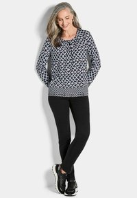 Langärmliges Oberteil in Marineblau mit geometrischem Muster, kombiniert mit schwarzen Slim-Fit-Hosen und schwarzen Sneakers mit weißen Akzenten.