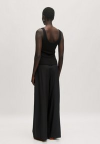 Zwarte aansluitende tanktop gecombineerd met wijde zwarte broek. De stof lijkt glad met een subtiele textuur, en het ontwerp heeft een ronde halslijn.