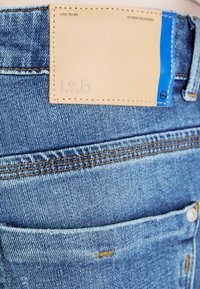 Jeans i denim med en ljusblå färg, textil med struktur och en läderlapp med präglad text. Påtaglig sömnad och detalj vid fickorna.