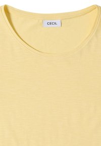 T-shirt jaune à col rond avec manches courtes et une étiquette blanche avec le nom de la marque "CECIL" à l'intérieur du col.