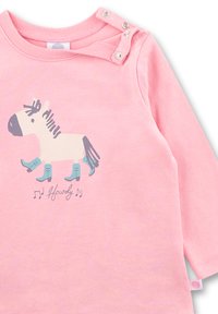 Helles rosa Langarmshirt mit einem weißen Pferdemotiv, das blaue Stiefel trägt. Verfügt über Druckknöpfe an der linken Schulter.