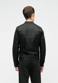 Giacca in pelle nera con una texture liscia, design con colletto e spalle cucite, indossata su jeans scuri. Semplice e con una silhouette aderente.