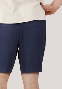 Mörk marinblå shorts i bomull, med rak skärning, två bakfickor och en slät yta. Bärs med en ljusfärgad skjorta.