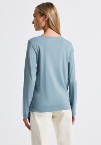 Long-sleeve shirt in light blue cotton with a round neckline and a relaxed fit. Soft texture, subtle stitching details at the hem.