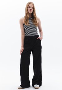Zwarte wijde broek met zijzakken, gecombineerd met een zwart-wit gestreepte tanktop. Beschikt over een soepele textuur en een relaxed fit, gestyled met sneakers.