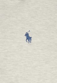 Jasnoszara bawełniana koszulka z małym niebieskim haftowanym logo gracza w polo po lewej stronie klatki piersiowej. Miękka tekstura o klasycznym kroju.