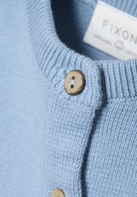 Ljusblå tröja i ekologisk bomull med ribbat halsband och detaljer i träknapp, som visar ett strukturerat stickat mönster.