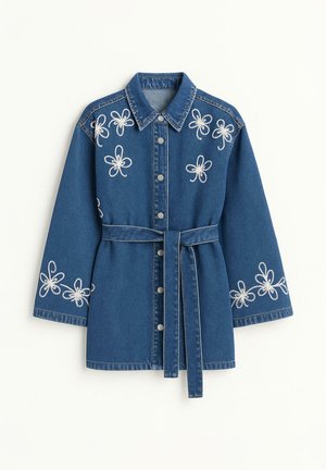 Gombos elől záródó farmerdzseki derékövvel, fehér hímzett virágmintákkal a vállakon és az ujjakon.