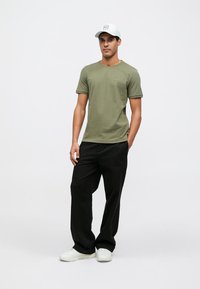 Oliiviroheline T-särk lühikeste varrukatega, ümara kaelusega, õrn logo, kombineeritud mustade lahtiste pükstega ja valgete tossudega. Komplekti täiendab nokamüts.