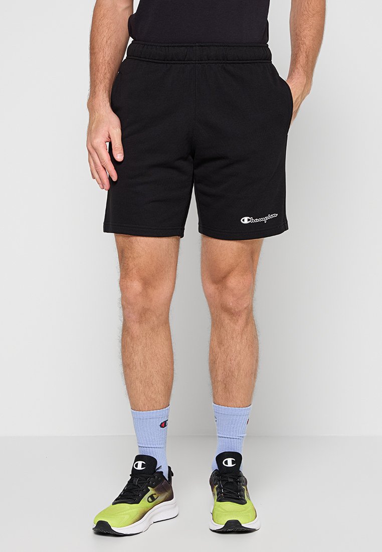 Pantalones cortos deportivos negros con una cintura elástica y un logo en la parte inferior izquierda. El material parece suave y transpirable, adecuado para ropa activa.