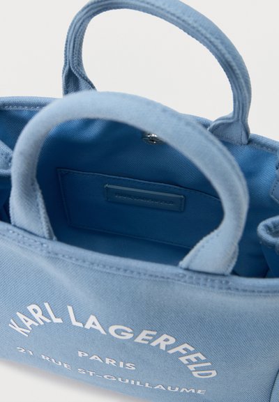 Светлосиня чанта Karl Lagerfeld с къси дръжки и бял напис, показваща отворения интериор и вътрешен джоб.