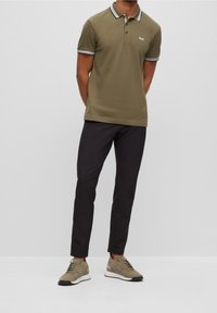 Polo vert olive avec col et manches à rayures blanches contrastantes, associé à un pantalon noir fuselé et des baskets kaki.