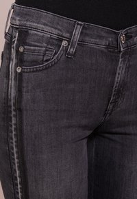 Ciemnoszare dżinsy o wąskim kroju, z błyszczącymi metalowymi akcentami, klasycznym pięcio-kieszeniowym designem oraz delikatnym wyblaknięciem wzdłuż szwów.