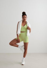 Limegroene sportoutfit bestaande uit een cropped top en high-waisted shorts. Witte handdoek over de schouders, gecombineerd met witte sneakers en sokken.