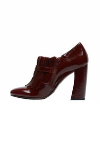 Scarpa con tacco alto in vernice rossa, punta appuntita, dettagli con frange e cerniera laterale. Presenta un tacco spesso e una texture liscia.