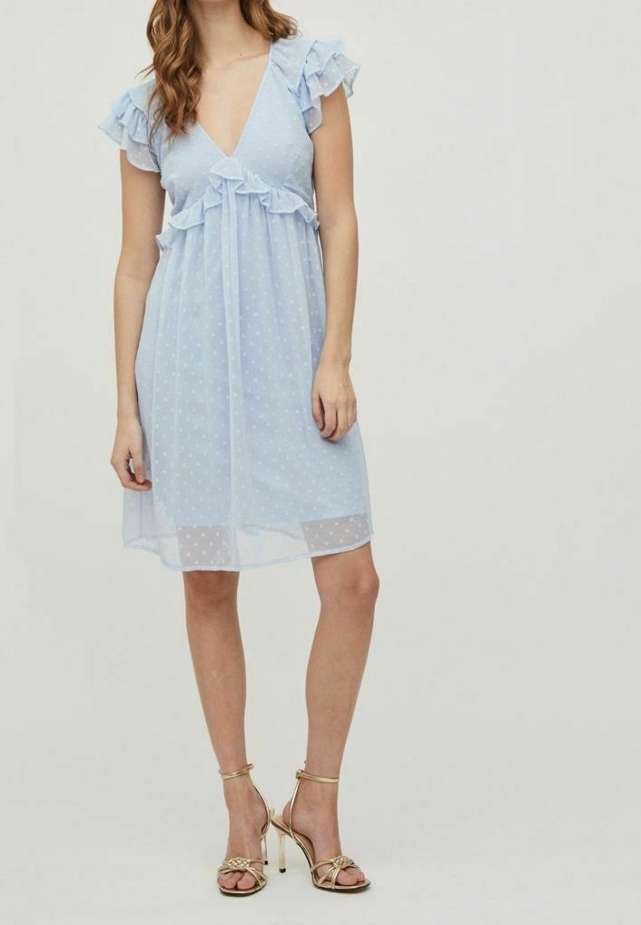 Ljust blå klänning med prickar, volangärmar och djup v-ringning. Genomskinligt tyg med avslappnad passform och knälång längd. Guld sandaler.