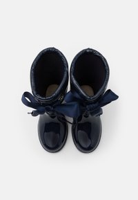 Bottes imperméables brillantes bleu marine avec un intérieur douillet, un accent en tissu en forme de nœud en haut et un design à bout arrondi.