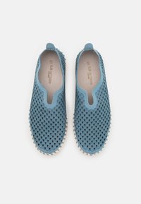 Zapatos azul claro sin cordones con un upper texturizado que presenta cortes circulares, aberturas elásticas y una suela de goma con pequeños acentos redondos.
