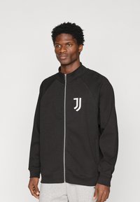 Felpa nera con zip e maniche raglan, con logo bianco sul lato sinistro del petto. Texture morbida con polsini e orlo a coste.