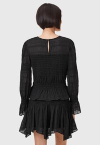 Schwarzes Kleid mit strukturierter Baumwolle, gerafftem Oberteil, langen Ärmeln, Rüschensaum und Rückenschlitz mit Schlüsselöffnungs-Design.