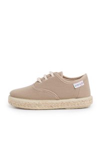 Beige canvas lace-up shoe with woven jute sole and a small fabric tag stitched near the heel on a white background.