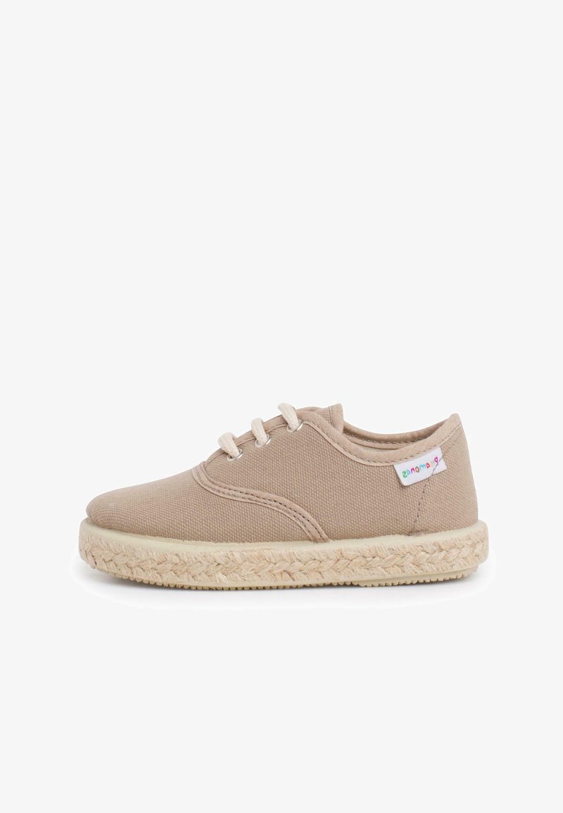 Beige canvas lace-up shoe with woven jute sole and a small fabric tag stitched near the heel on a white background.