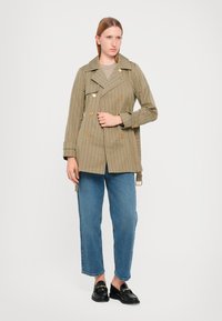 Khaki-gepatroonde trenchcoat met een dubbelgeknoopte ontwerp, opvallende kraag en gouden knopen, gecombineerd met blauwe rechtgesneden jeans.