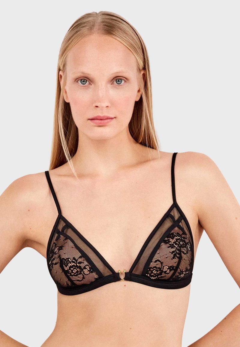 Bralette triangular de encaje negro con paneles de malla transparente, tirantes finos y un acento decorativo de hardware dorado en el centro frontal.