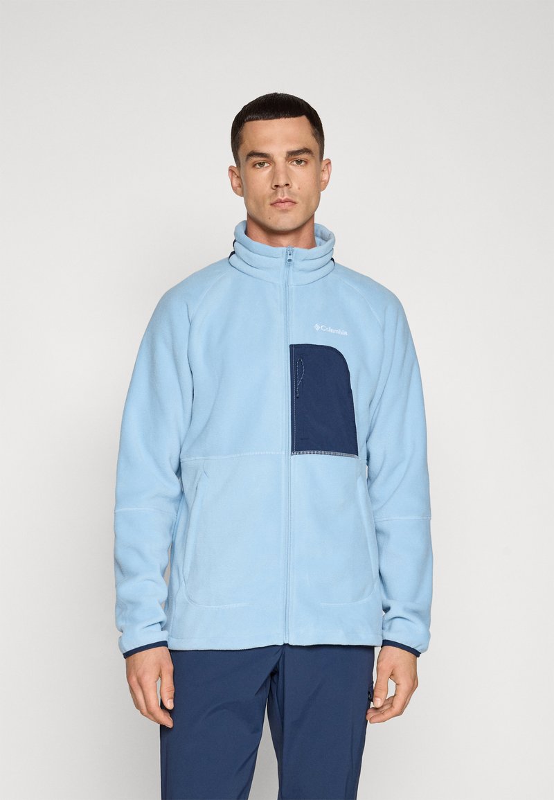 Jasnoniebieska polarowa kurtka z wysokim kołnierzem, zamek błyskawiczny z przodu oraz granatową kieszenią na piersi. Miękka tekstura z płaskimi szwami.