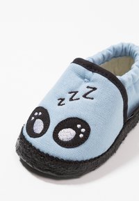 Světle modrá textilní bačkora s černou podrážkou, na přední straně s velkými vyšitými kreslenými očima a nápisem "zzz". Elastický vršek pro snadné obouvání.