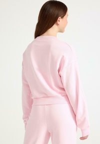 Rosa sweatshirt i mjukt tyg med avslappnad passform, ribbade ärmslut och rundad halsringning. Bakifrån visas en enkel, slät design.