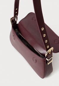 Bordeaux lederen handtas met een platte vorm, verstelbare schouderband en gouden hardware. Het interieur heeft een gladde voering en een ritsvak.