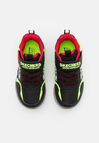Sapatos Skechers pretos e verde néon com um upper texturizado, interior vermelho, atacadores elásticos e colarinhos almofadados, com o rótulo "RESISTENTE À ÁGUA".