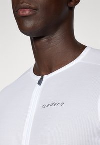 Weißes Fahrradtrikot mit Reißverschluss und grauen Akzenten. Hergestellt aus atmungsaktivem, strukturiertem Stoff und mit einem Logo auf der Vorderseite.