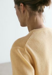Yellow knitted sweater with a smooth texture, featuring a rounded neckline and visible seams at the shoulders, shot from the back.
