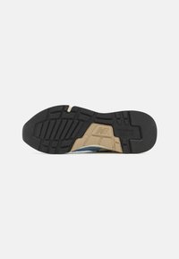 Sole in gomma nera con motivo a rilievo, con una intersuola beige e una tomaia blu, che mostrano una combinazione di materiali e strati di design.