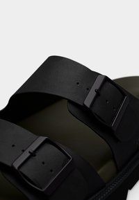 Τα μαύρα σανδάλια διαθέτουν δύο φαρδιές λουράκια με υφασμάτινα σχέδια, ρυθμιζόμενες αγκράφες και ανάγλυφη εσωτερική σόλα για άνεση.