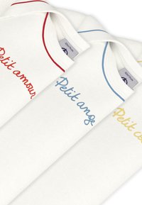 Τρία λευκά παιδικά T-shirts με στρογγυλές λαιμόκοψεις. Κάθε ένα έχει κεντημένες φράσεις: κόκκινο «Petit amour», μπλε «Petit ange» και κίτρινο «Petit cœur».
