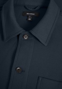 Donkerblauw overhemd met knopen en kraag, twee zwarte knopen en zichtbaar Matinique merklabel binnenin de halslijn.