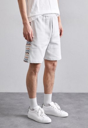 Grå bomullsshorts med ribbad midja och sidodetaljer i zigzag-mönster i blått, orange och gult; använda med vita sneakers och strumpor.