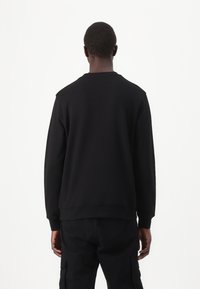 Sudadera negra con mangas largas, diseño de cuello redondo y puños acanalados. La tela parece suave y de peso medio, mostrando un color sólido.