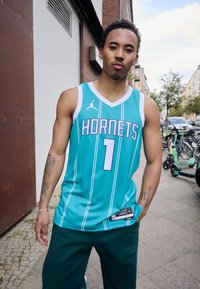 Teal basketballtrøje med "HORNETS" i hvide bogstaver og lilla accenter, der har et Nike-logo og lodret stribedesign.