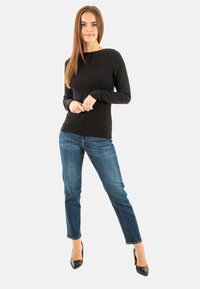 Maglione nero a maniche lunghe con sottili scintille, abbinato a jeans blu slim-fit e tacchi alti neri, su sfondo bianco.
