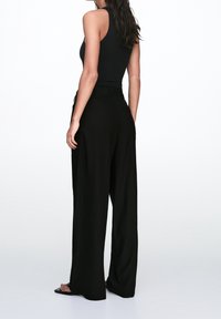 Czarne spodnie typu wide-leg o gładkiej fakturze, wysokim stanie i ozdobnym pasku. W komplecie dopasowany czarny top na ramiączkach w eleganckim stylu.
