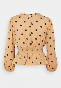 Beige långärmad blus med svarta prickar, elastisk midja, peplumkant, knäppt nyckelhål baktill och draperade manschetter.