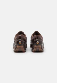 Brown athletic shoes with textured mesh upper, glossy accents, and rubber outsole. Features padded collar and logo on the heel.