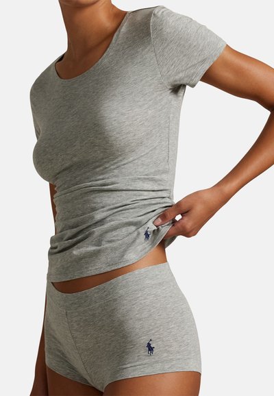 Γυναίκα που φοράει γκρι εφαρμοστό τοπ με κοντά μανίκια και ταιριαστά σορτς τύπου boyshort, και τα δύο με μικρά σκούρα μπλε κεντημένα λογότυπα στην αριστερή πλευρά.